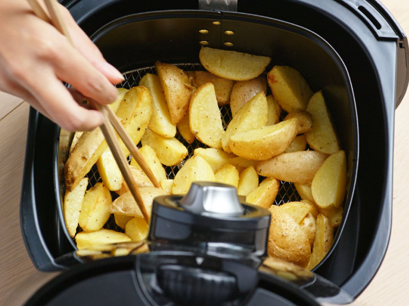 mulher fazendo batatas rusticas em casa na airfryer