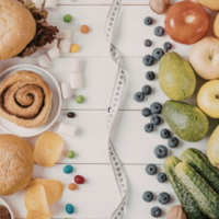 Comparação entre alimentos ultraprocessados, como hambúrguer e doces, e alimentos naturais, como frutas e vegetais, divididos por fita métrica sobre mesa branca.