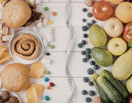 Comparação entre alimentos ultraprocessados, como hambúrguer e doces, e alimentos naturais, como frutas e vegetais, divididos por fita métrica sobre mesa branca.